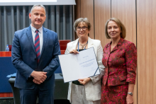 A man and two women are posing together for a photo. The woman in the middle is holding an open diploma in her hands.