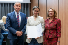 A man and two women are posing together for a photo. The woman in the middle is holding an open diploma in her hands.