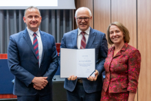 Two men and a woman are posing together for a photo. The man in the middle is holding an open diploma in his hands.
