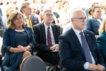 A close-up of participants seated on chairs and listening to a presentation. People in the front row are holding notebooks and sheets of paper.