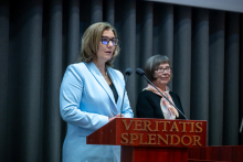 Two people standing behind a podium with microphones. The person in the foreground is speaking, while the second person stands slightly behind, listening.