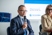 Two people are seated side by side; one person is holding a microphone while speaking, with “Pharmaceris” and “INFARMA” logos and boxes visible in the background.