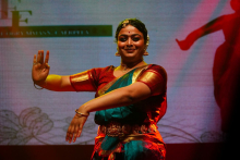 A solo performer on stage wearing a colorful traditional outfit, holding arms in a stylized dance pose.