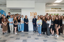 Large group of people standing in a hallway in front of a wall with the inscription “102 Years of the Faculty of Pharmacy.” Some participants are holding folders or glass awards.