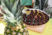A tray filled with several dozen chocolate balls is placed on a table. In the foreground, part of a pineapple is visible