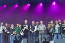Kilkunastoosobowa grupa stoi na scenie podczas wydarzenia plenerowego. Część osób trzyma duże, symboliczne klucze.
