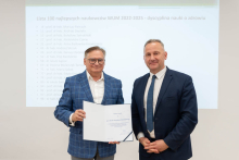 Dwóch mężczyzn pozuje do zdjęcia. Jeden trzyma w rękach otwarty dyplom.