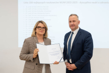Kobieta i mężczyzna pozują do zdjęcia. Kobieta trzyma w rękach otwarty dyplom.