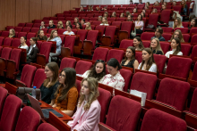 Widok sali wykładowej wypełnionej uczestnikami. W większości są to kobiety siedzące na czerwonych fotelach i skierowane w stronę sceny.