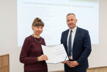 Kobieta i mężczyzna pozują do zdjęcia. Kobieta trzyma w rękach otwarty dyplom.