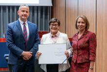 Mężczyzna i dwie kobiety pozują razem do zdjęcia. Kobieta pośrodku trzyma w rękach otwarty dyplom.