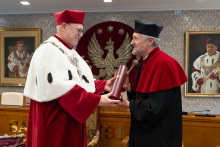 Rektor przekazuje dokument doktorowi honoris causa. Obaj ubrani są w togi akademickie.