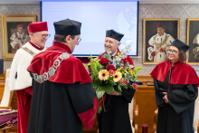 Cztery osoby stoją blisko siebie. Jedna osoba trzyma duży bukiet kwiatów. Pozostałe osoby stoją naprzeciw i patrzą na nią.