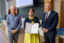 Two men and a woman stand together, the woman holds an open diploma in her hands.