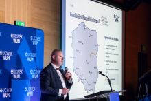 One person stands at a podium and speaks while holding a microphone. A map of Poland and the text “Polish Clinical Research Network” are displayed on the screen.