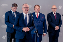 Four people stand by a microphone during a speech. A backdrop with the Medical University of Warsaw logo is visible in the background.