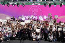 A group of several dozen people stands on stage holding diplomas raised up. In the background, there is a large screen with the text “Srebrne Wilki” and a graphic of a wolf’s head.