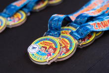 Medals lie on a dark surface. Each medal has a blue ribbon and the text “Dzień Dziecka Zawody Pływackie 2026” along with an illustration of children.