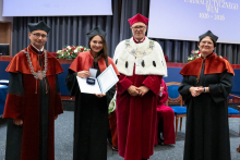  Four people stand on stage. One person holds a document and a case. Behind them, a screen displays “Faculty of Pharmacy WUM 1926–2026”.
