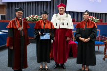  Four people stand on stage. One person holds a document and a case. Behind them, a screen displays “Faculty of Pharmacy WUM 1926–2026”.
