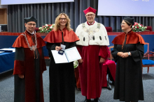  Four people stand on stage. One person holds a document and a case. Behind them, a screen displays “Faculty of Pharmacy WUM 1926–2026”.