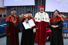  Four people stand on stage. One person holds a document and a case. Behind them, a screen displays “Faculty of Pharmacy WUM 1926–2026”.