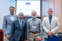 Four people stand side by side on stage for a photo. One holds a red notebook and another holds a blue folder. Behind them, a large screen displays the text “ACCORD Interdisciplinary Conference on Drug Sciences” along with the logos of the Medical University of Warsaw and the Faculty of Pharmacy.