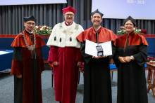 Four people stand on stage. One person holds a document and a case. Behind them, a screen displays “Faculty of Pharmacy WUM 1926–2026”.