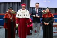  Four people stand on stage. One person holds a document and a case. Behind them, a screen displays “Faculty of Pharmacy WUM 1926–2026”.
