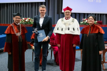  Four people stand on stage. One person holds a document and a case. Behind them, a screen displays “Faculty of Pharmacy WUM 1926–2026”.