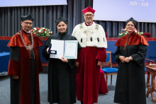  Four people stand on stage. One person holds a document and a case. Behind them, a screen displays “Faculty of Pharmacy WUM 1926–2026”.
