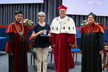  Four people stand on stage. One person holds a document and a case. Behind them, a screen displays “Faculty of Pharmacy WUM 1926–2026”.
