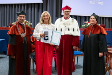  Four people stand on stage. One person holds a document and a case. Behind them, a screen displays “Faculty of Pharmacy WUM 1926–2026”.