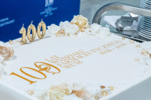 A cake with the inscription “100 years of the Faculty of Pharmacy WUM 1926–2026” placed on a table. The cake is decorated with ornaments and candles shaped as the number 100.