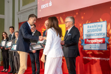 A man and a woman shake hands on stage during the presentation of awards, with other certificate recipients standing in the background.