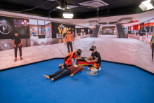 Two people wearing virtual reality headsets conduct a medical emergency simulation on a manikin lying on the floor in a virtual indoor environment.