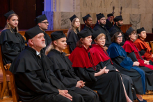 Women and men in academic robes sit on stage during a graduation ceremony.