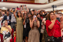 Family members and guests stand in the auditorium and take photographs with their mobile phones during the graduation ceremony.