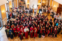 Graduates, university officials and guests gather in a hall. Several graduates throw their caps into the air while celebrating the completion of their studies.