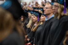 A group of people dressed in black academic gowns is standing in several rows, looking straight ahead.