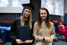 Two people are posing for a photo after the graduation ceremony. One of them is holding a closed diploma.