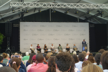 Uczestnicy konferencji siedzą przed sceną, na której odbywa się dyskusja panelowa prowadzona przez siedem osób.