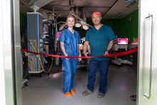 A group of medical staff and event participants pose for a group photograph in a conference room. A presentation screen about robotic surgery in children is visible in the background.