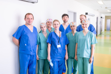 A group of medical staff wearing surgical scrubs pose for a group photograph in a hospital corridor.