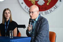 Dwie osoby siedzą przy stole konferencyjnym. Jedna z nich - dr hab. Tomasz Dzieciątkowski mówi do mikrofonu podczas panelu dyskusyjnego.