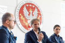 Trzy osoby uczestniczą w panelu dyskusyjnym. Jedna z nich wypowiada się do mikrofonu.