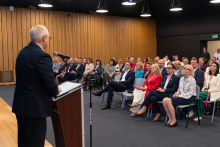 Osoba odczytuje dokument przy mównicy podczas uroczystości Uniwersyteckiego Centrum Klinicznego WUM.