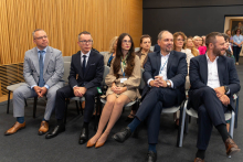 Pięć osób siedzi w pierwszym rzędzie podczas uroczystości. W tle znajdują się pozostali uczestnicy wydarzenia.