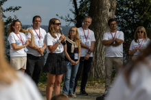 A participant speaking into a microphone while organizers stand nearby during an outdoor meeting.