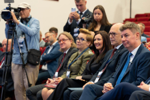 Conference attendees and media representatives seated in the front rows of an auditorium during the event.